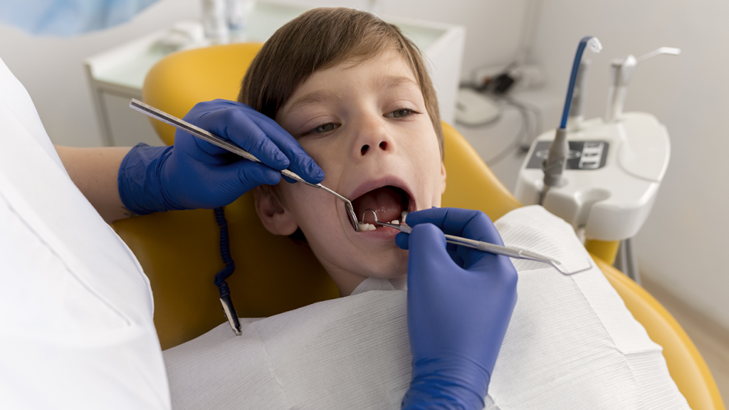 Criança na cadeira do dentista com a boca aberta enquanto é avaliado pelo odontopediatra.