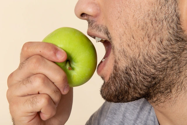 Homem comendo uma maça verde, um dos tipos de alimentos detergentes.